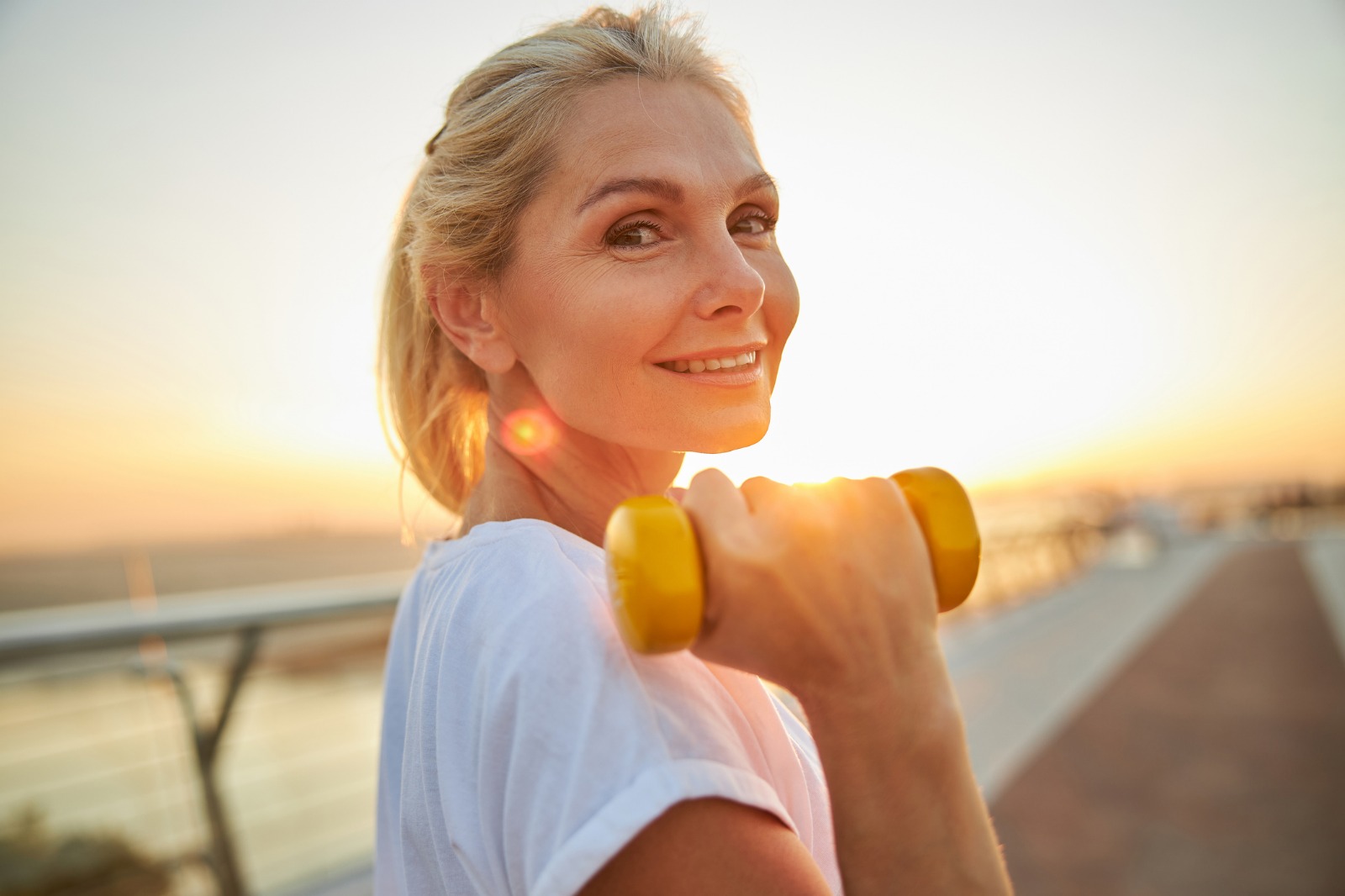 Woman lifting yellow weights outdoor during sunset
