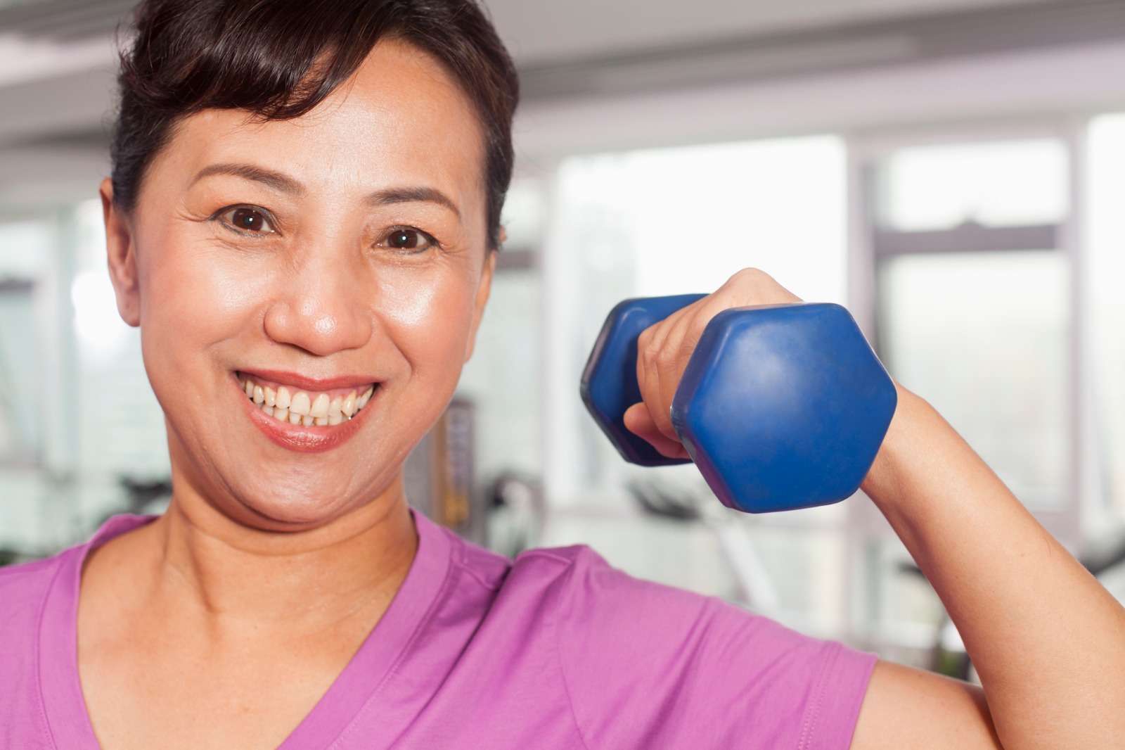 Women in 50s lifting blue dumbbell in a gym